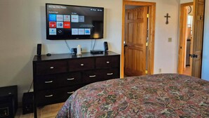Una camera da letto con un letto, una TV a muro che mostra l'interfaccia di un lettore DVD, una sveglia e una porta in legno.
