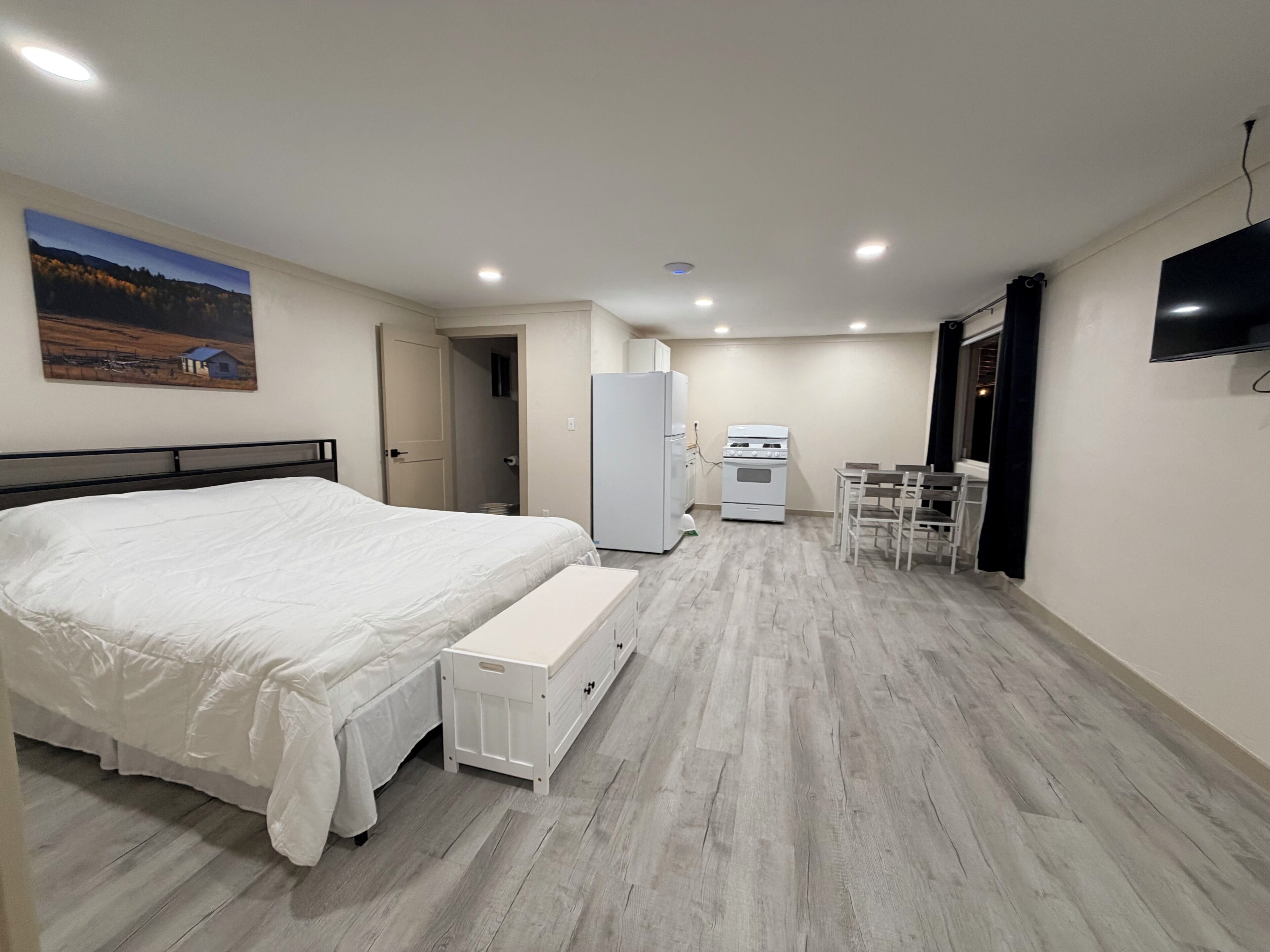 A bedroom with a bed, bedside table, and a small kitchenette with a fridge and stove.