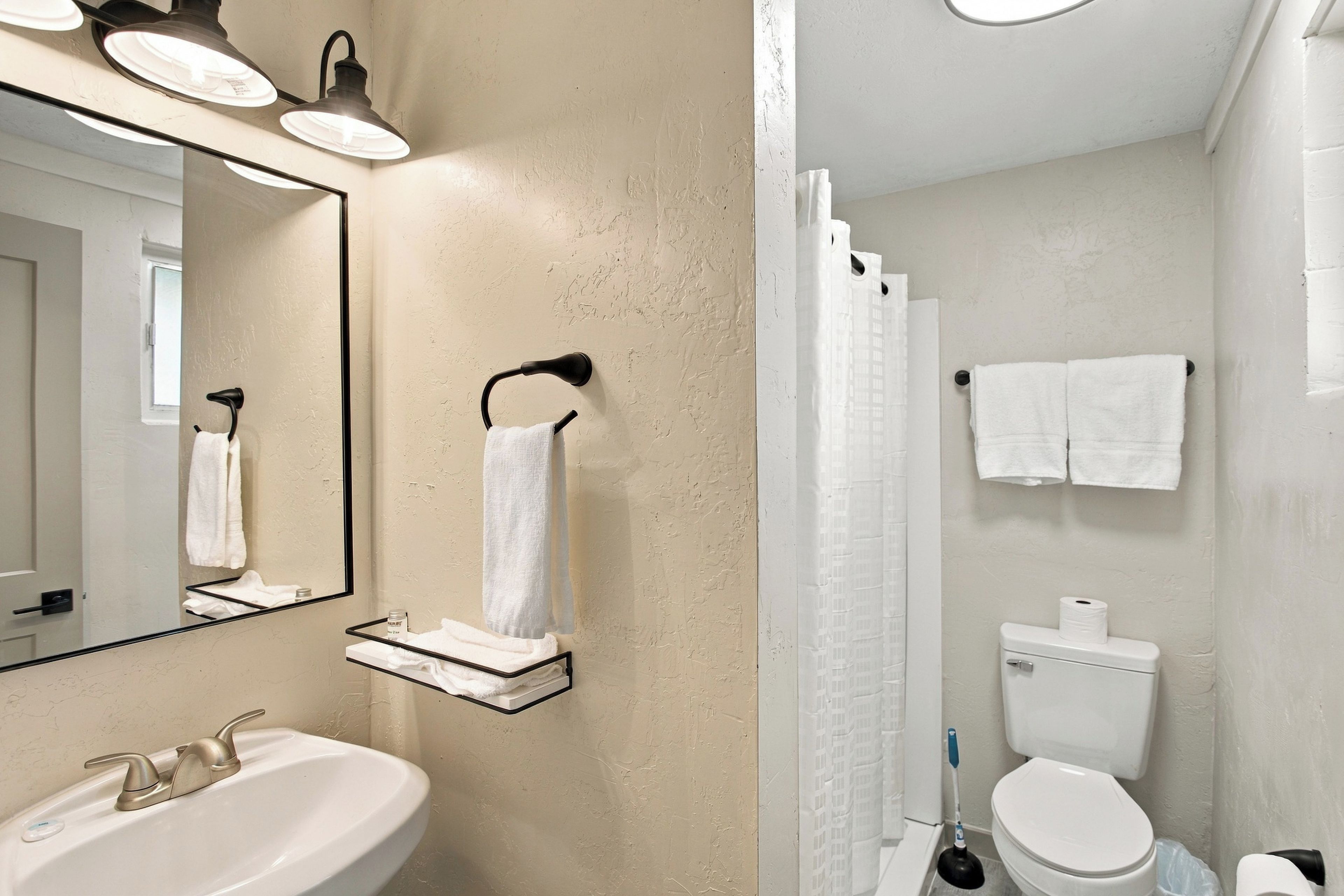 A bathroom with a sink, mirror, towel rack, toilet, and shower curtain.