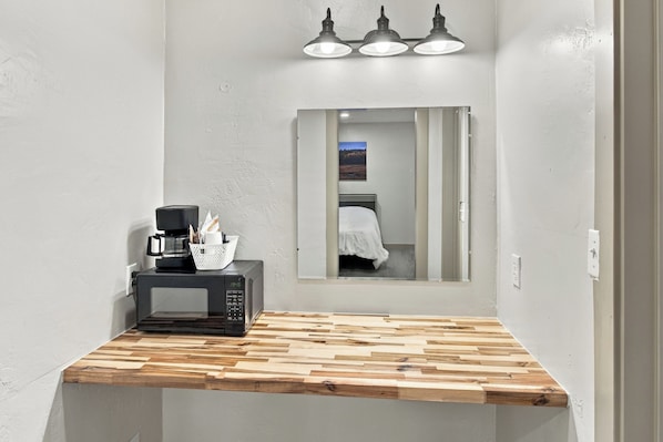 A small kitchenette with a microwave, coffee maker, and a basket on a wooden countertop.