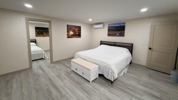 A bedroom with a bed, a bench, two wall-mounted air conditioners, and two framed pictures.
