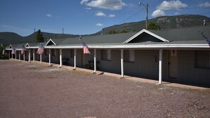 A row of motel buildings with American flags, a gravel parking area, and a mountainous backdrop.