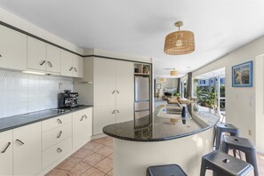 Une cuisine moderne dotée d’un îlot central aux lignes courbes, de meubles blancs et d’un luminaire suspendu.