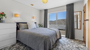 Un dormitorio con cama, lámparas de noche, una ventana con cortinas, una planta y vistas al exterior.