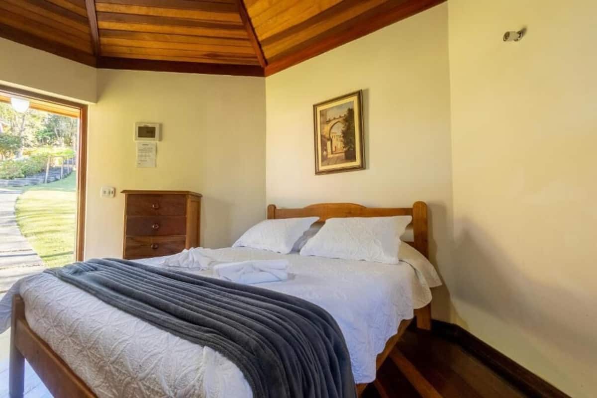 Un dormitorio con cama de madera, mesita de noche, cómoda, un cuadro enmarcado en la pared y una puerta que da a un jardín.