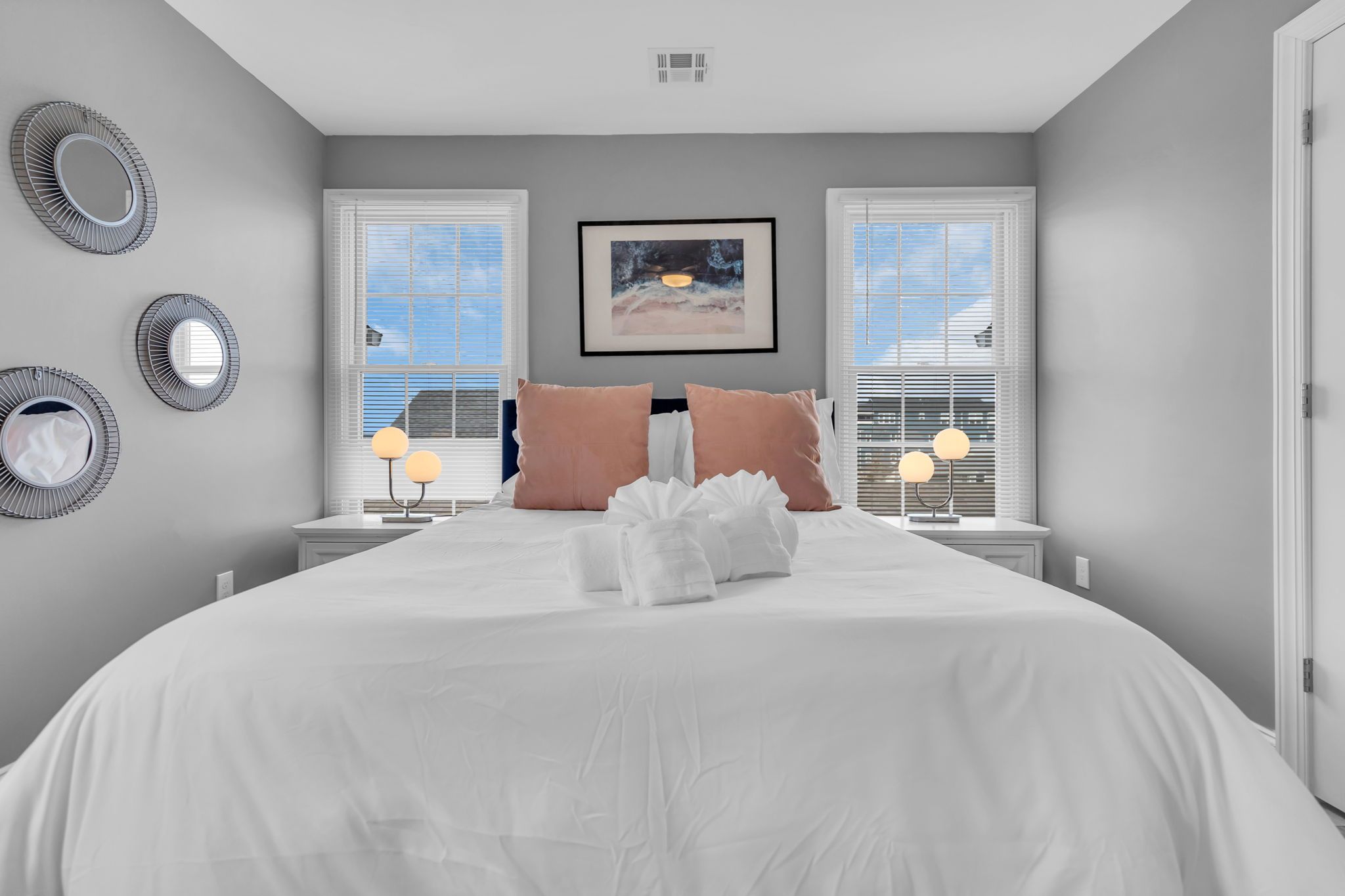 Una camera d'albergo con un letto grande, due comodini, un quadro appeso al muro e una finestra con tende.