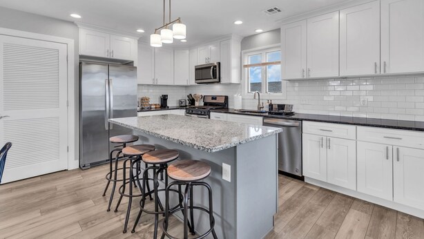 Una cocina moderna con armarios blancos, un refrigerador de acero inoxidable, una isla de granito con taburetes y luces empotradas.