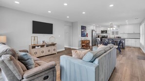 Una sala de estar moderna con un sofá, una televisión y una zona de cocina al fondo.