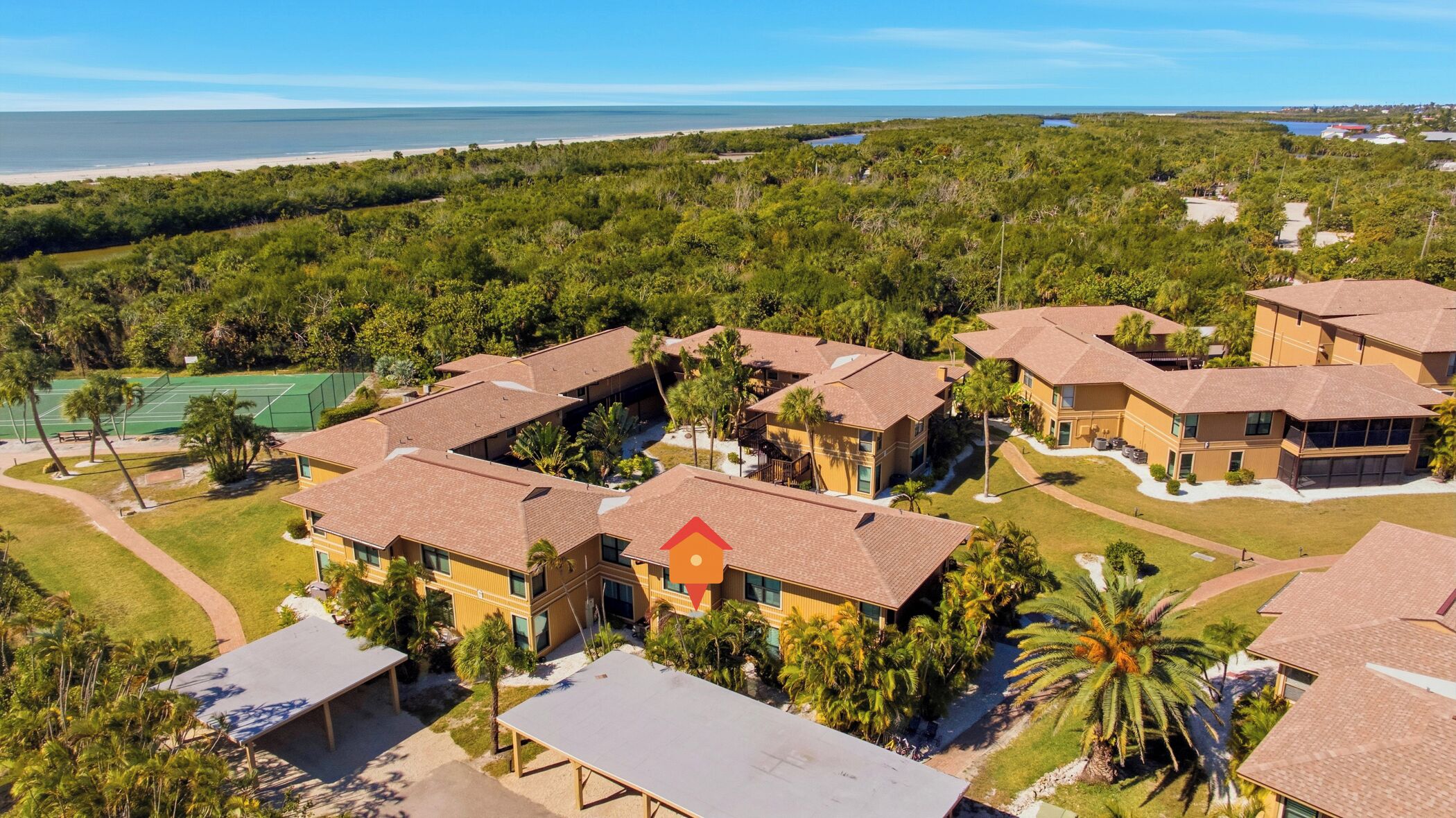 Zona residencial con varias casas de dos pisos, una cancha de tenis y una playa al fondo.