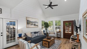 A spacious living room with a dark sofa, striped chairs, a wooden coffee table, and a ceiling fan.