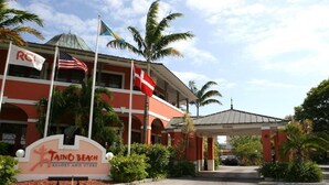 Taino Beach Resort and Club, un edificio rojo, palmeras y varias banderas, incluyendo la bandera estadounidense.