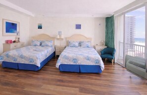 Ein Zimmer mit zwei Betten, einem Sessel, einem Nachttisch, einer Lampe und Meerblick.