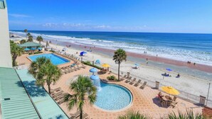 A pool area with a water feature, beach chairs, umbrellas, and a view of the ocean. - Oceanfront Condo Daytona Beach (Daytona Beach)