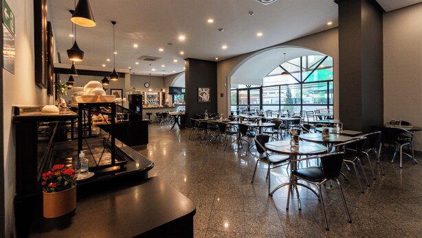 A spacious cafe with multiple tables and chairs, a coffee bar, and large windows allowing natural light. - RCT Hospedagens - Perdizes Palestra Itália (São Paulo)