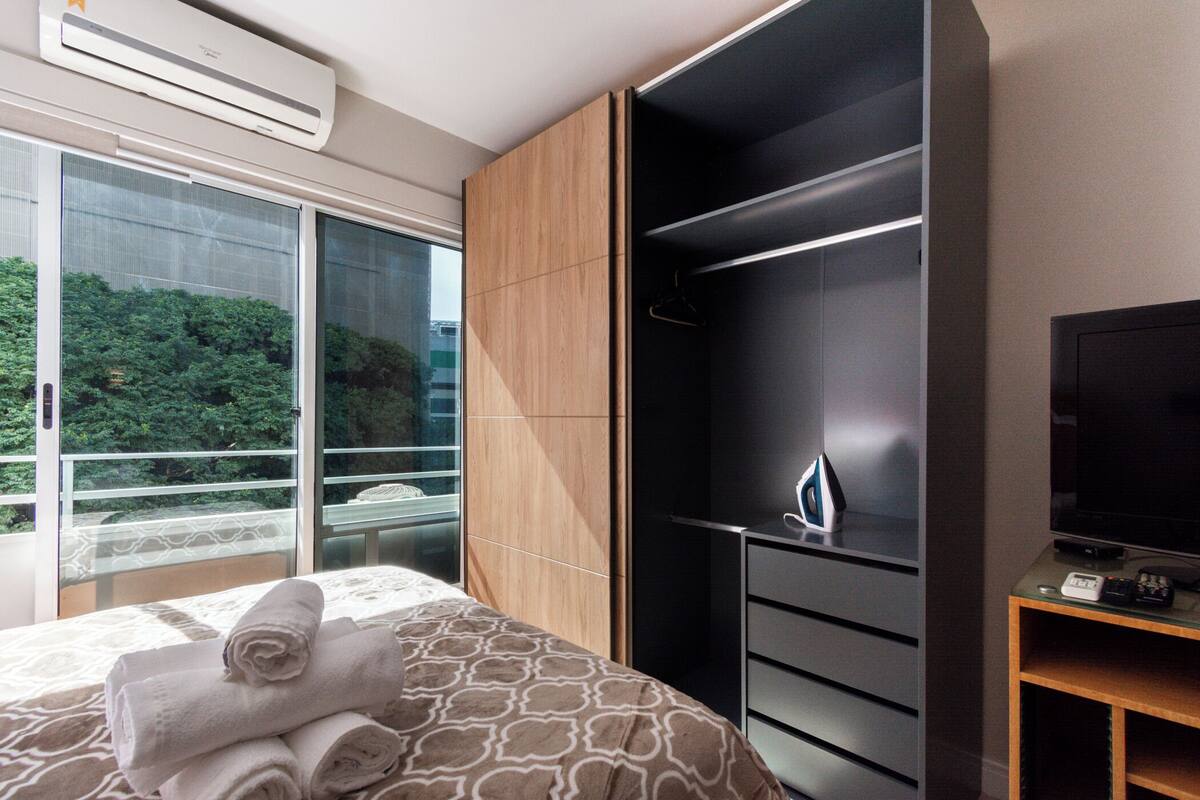 A hotel room with a bed, a TV, a wardrobe, and a balcony with a view of greenery.