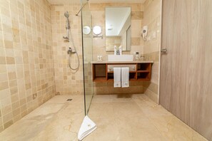 Un baño moderno con cabina de ducha de vidrio, tocador con espejo y estante de madera.
