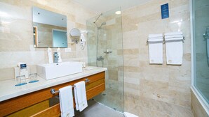 Een moderne badkamer met een douchecabine van glas, een grote spiegel, een witte wastafel en netjes opgevouwen handdoeken.