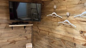 Un intérieur en bois avec un téléviseur fixé au mur, une petite étagère et des cintres blancs accrochés au mur.