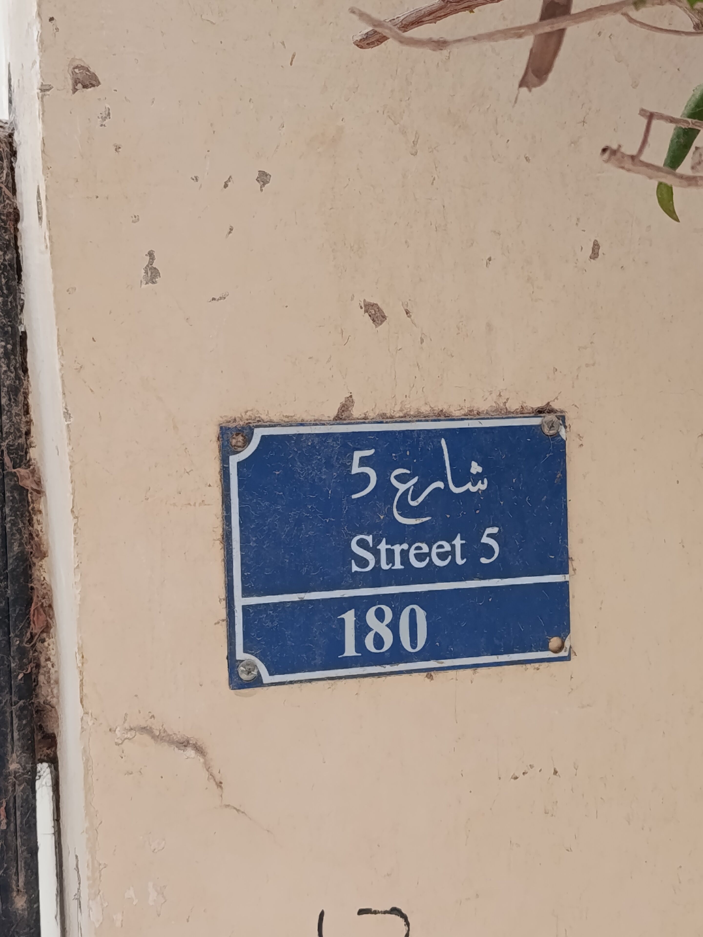 A blue street sign with white text indicating 'Street 5' and the number '180' on a beige wall.