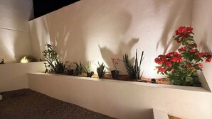 Eine weiße Wand mit einer Reihe von Topfpflanzen und einem kleinen Wasserspiel.