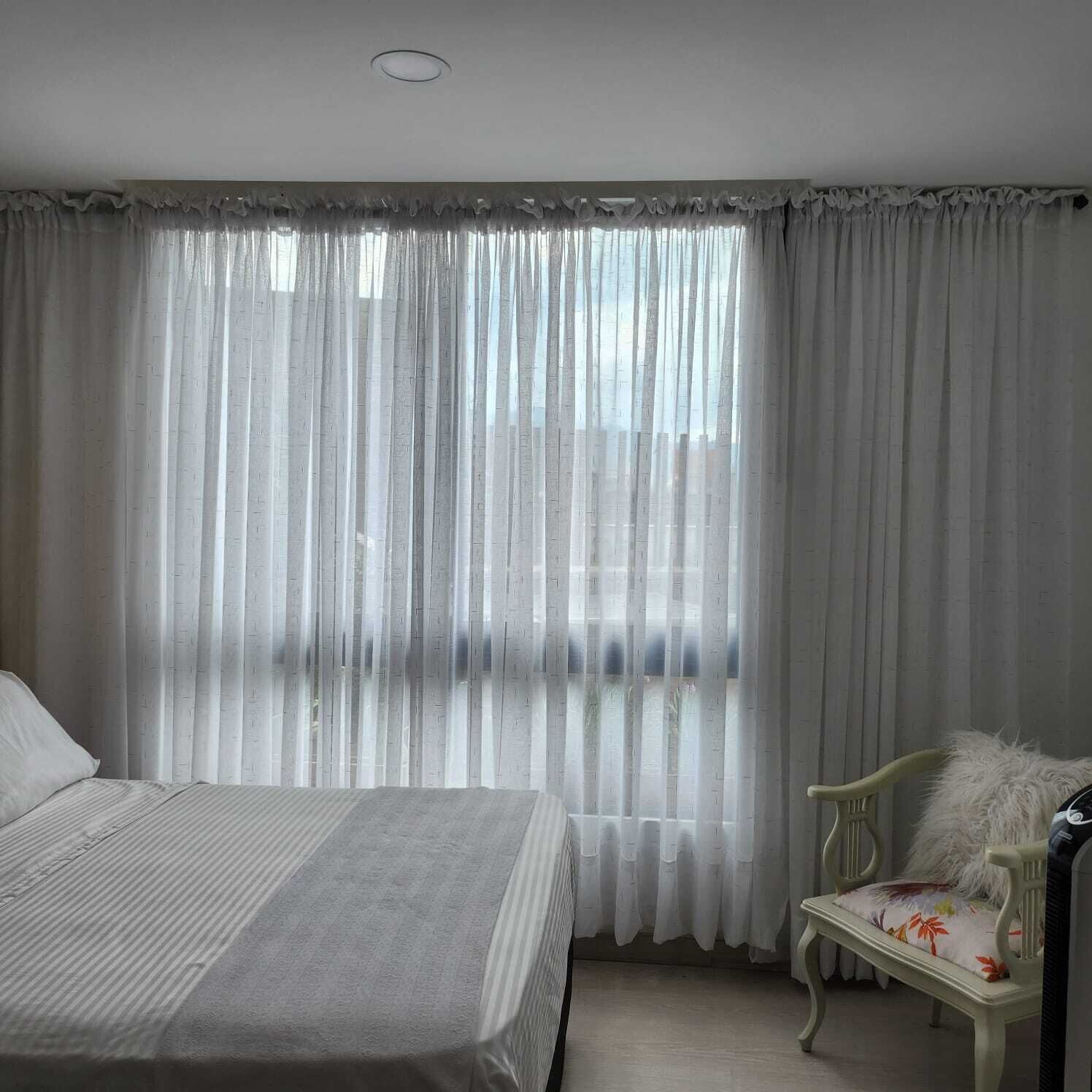 Une chambre à coucher avec un lit, une chaise et une fenêtre ornée de rideaux légers.