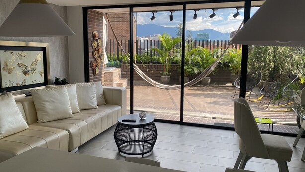 Ein modernes Wohnzimmer mit einer Couch, einem runden schwarzen Tisch und Blick auf eine Stadtlandschaft durch große Fenster.