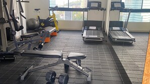 Ein Fitnessstudio mit Trainingsgeräten, Laufband und einem großen Fenster mit Blick auf die Stadt.