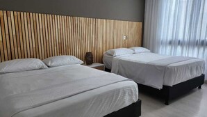 Ein Hotelzimmer mit zwei Betten, einem hölzernen Kopfteil, einem Nachttisch und einem Fenster mit Vorhängen.