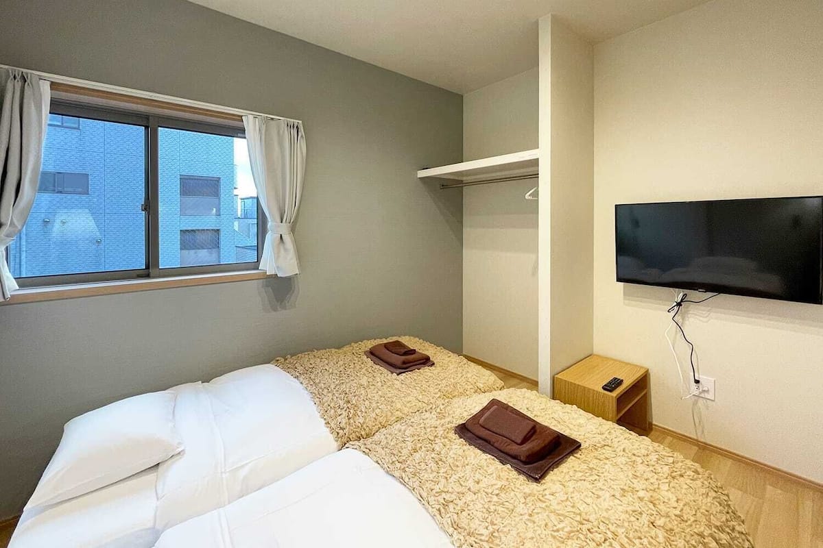 Habitación de hotel con cama, televisión, ventana con cortinas y una mesita de noche.