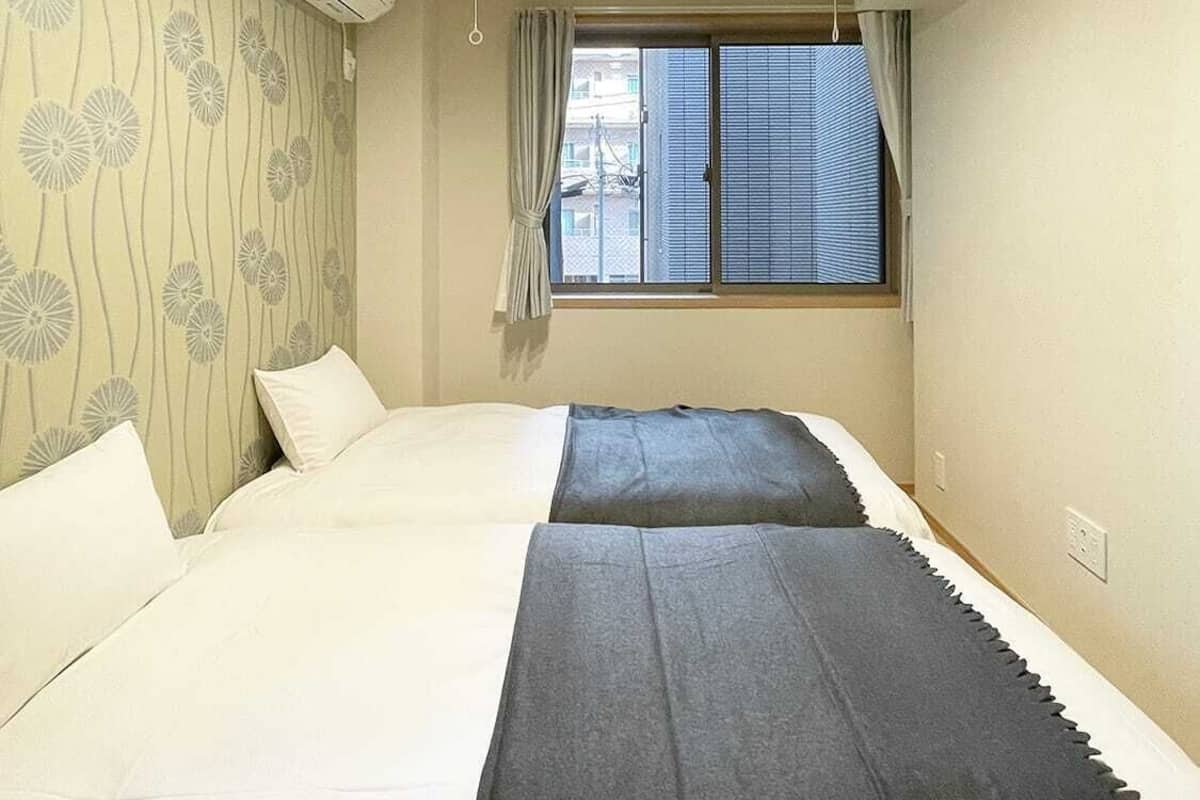 Habitación de hotel con dos camas, una ventana con cortinas, un equipo de aire acondicionado y una lámpara en el techo.