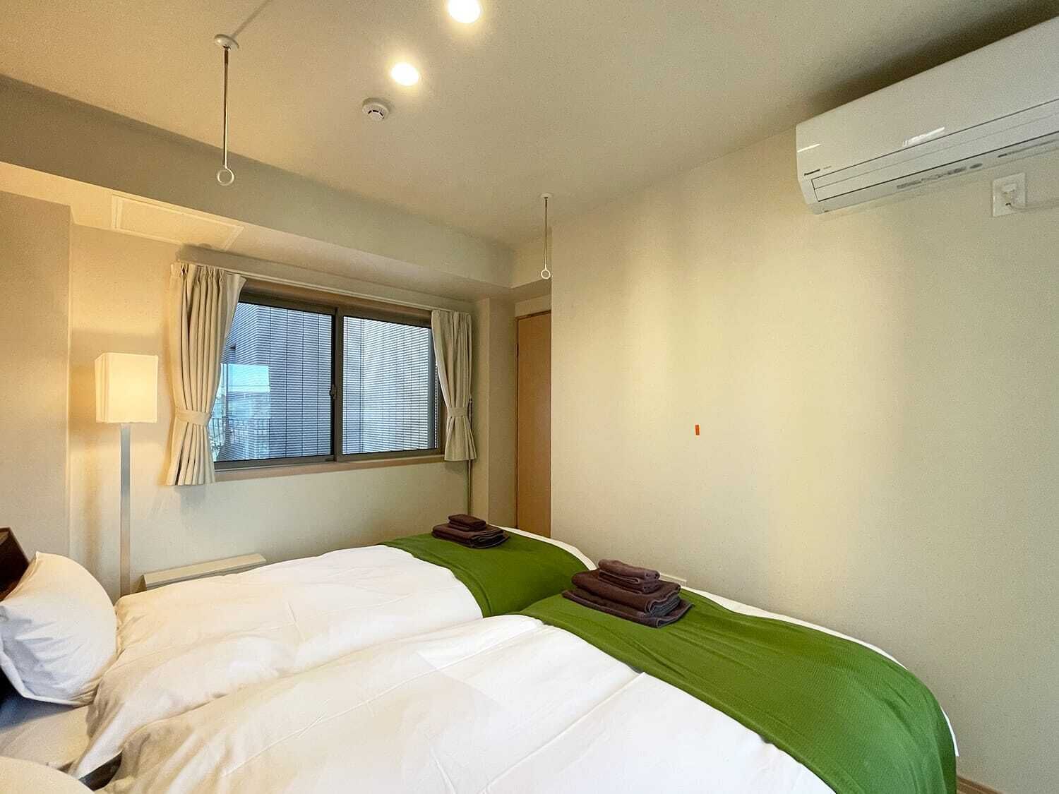 Habitación de hotel con dos camas, una ventana con cortinas, una lámpara de pie y un equipo de aire acondicionado.