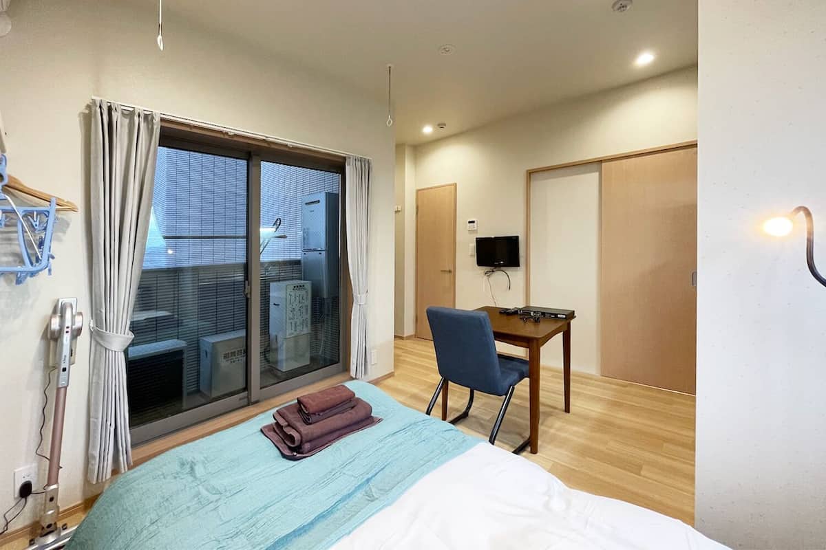 Habitación de hotel con cama, escritorio, silla, televisor y puerta corredera al exterior.