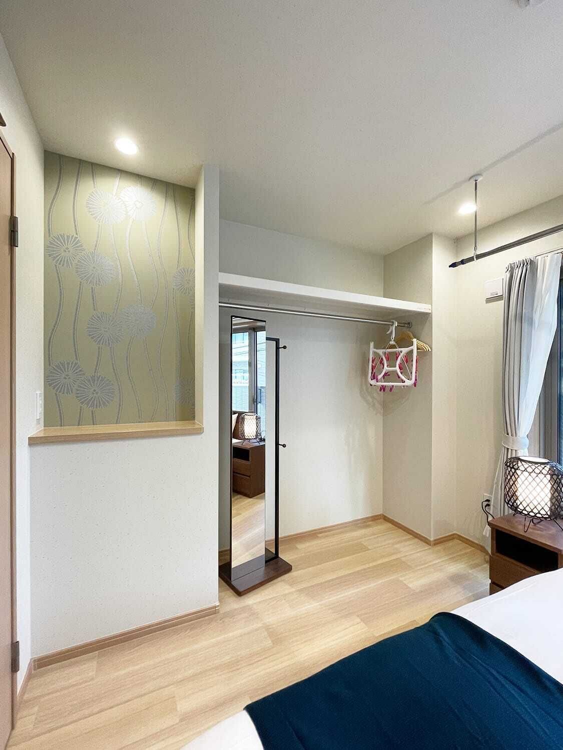A bedroom with a bed, a wardrobe, a mirror, a hanging light fixture, and a window with a floral pattern.