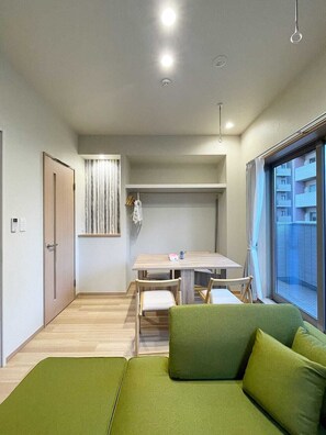 A compact living space with a dining area, a sofa, and a window with a view of buildings.