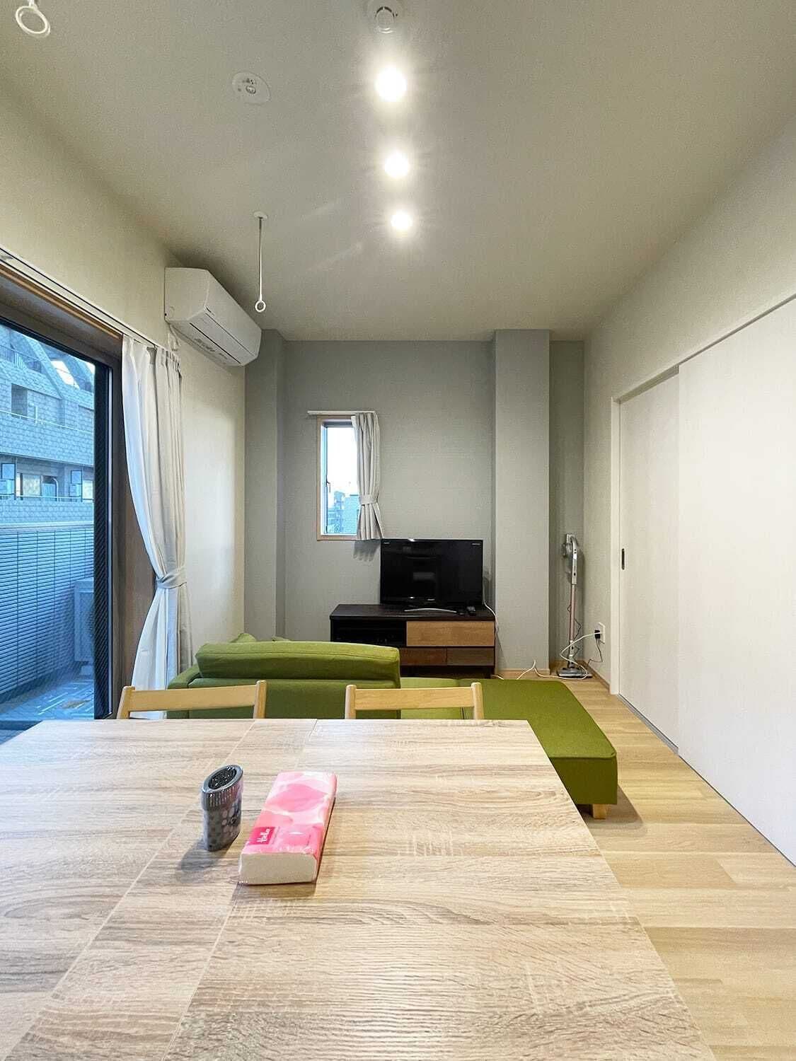 A modern living room with a wooden table, green sofa, and a TV.