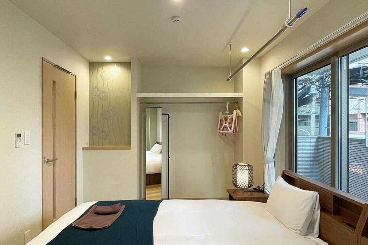 Habitación de hotel con dos camas, una ventana con persianas, una mesita de noche con lámpara y una puerta.