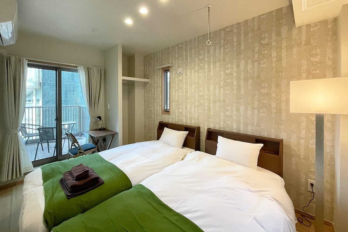 Habitación de hotel con dos camas, un balcón con una silla, una mesita y una lámpara.