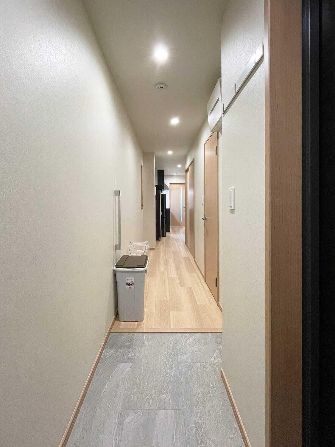 A hallway with a trash bin, wooden flooring, and doors on both sides.