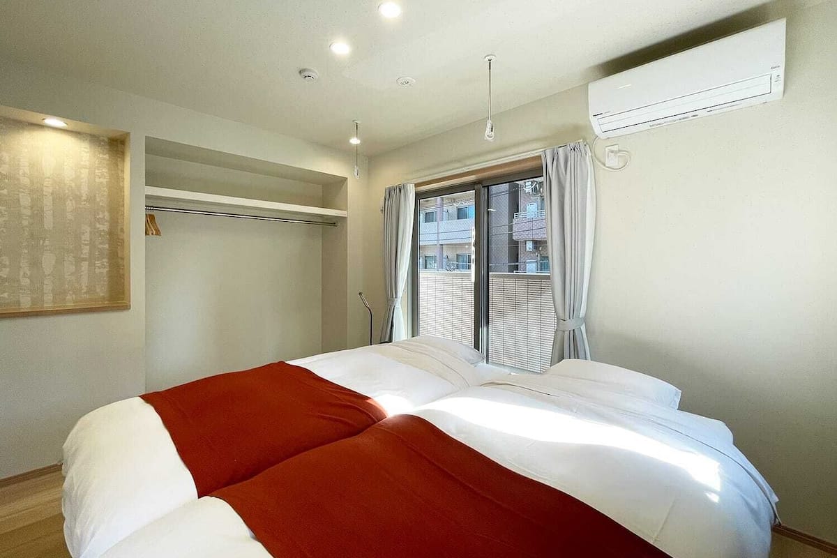 Una habitación de hotel con cama, aire acondicionado, ventana con persianas y una lámpara en el techo.