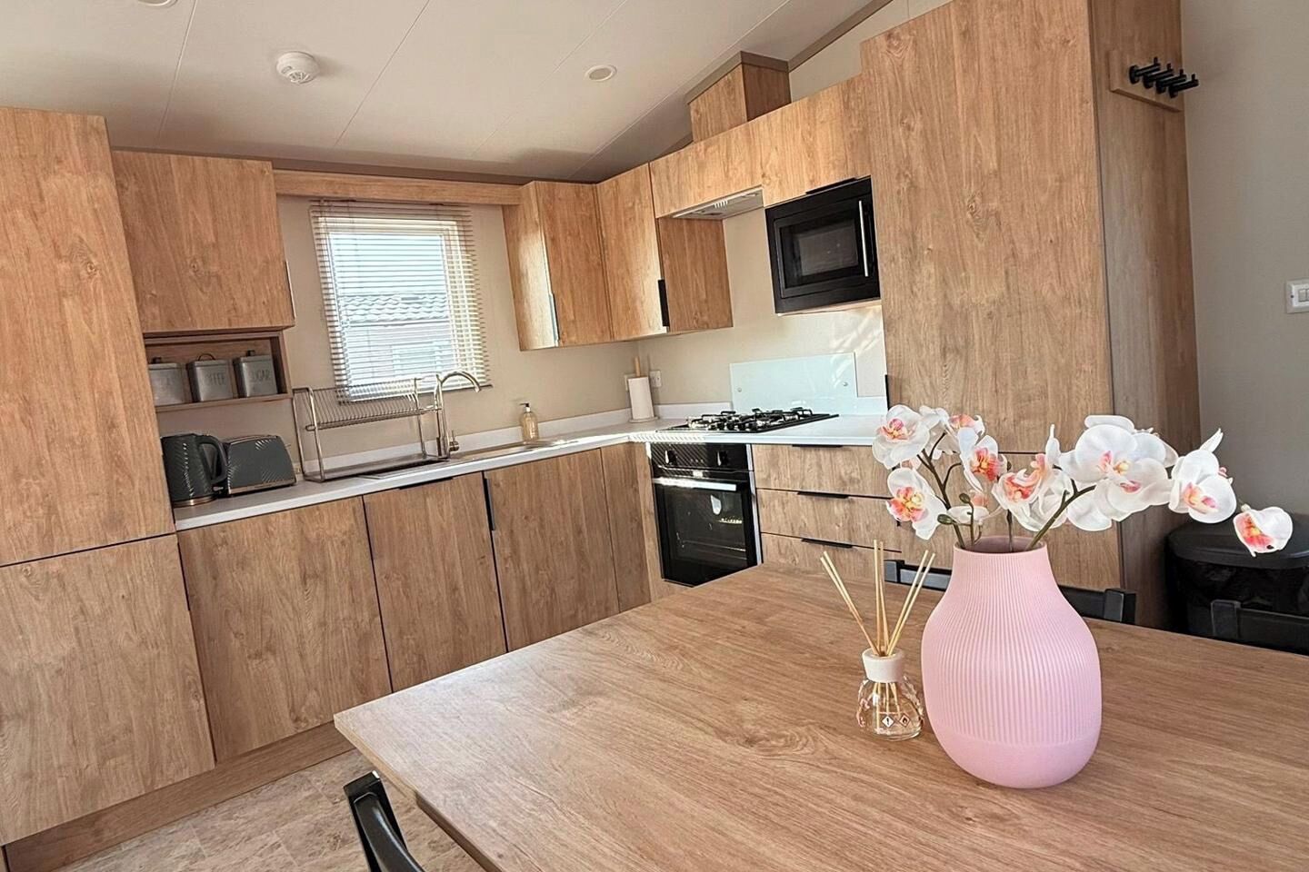Une cuisine moderne avec des meubles en bois, un évier en acier inoxydable et un vase rose orné de fleurs, posé sur le comptoir.