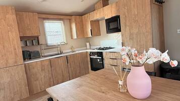 Une cuisine moderne avec des meubles en bois, un évier en acier inoxydable et un vase rose orné de fleurs, posé sur le comptoir.