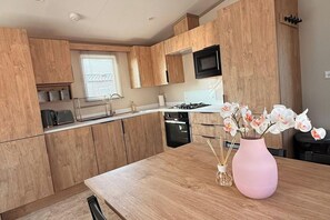 A modern kitchen with wooden cabinets, a stainless steel sink, and a pink vase with flowers on the counter. - 3-Bed - Sleeps 6 - Parking - Balcony (Malton)