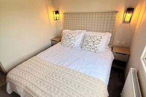 A neatly made bed with a quilted white duvet, two matching pillows, and a decorative throw at the foot. There are two bedside tables with lamps, and a radiator is visible on the right. - 3-Bed - Sleeps 6 - Parking - Balcony (Malton)