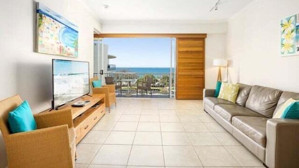 A living room with a television, a sofa, a coffee table, and a view of the ocean through a sliding door. - 1 Bedroom Balcony Poolside (Kings Beach)
