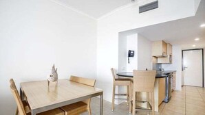 A compact kitchen with modern appliances, a dining area with a wooden table and chairs, and a small decorative fish on the table. - 1 Bedroom Balcony Poolside (Kings Beach)