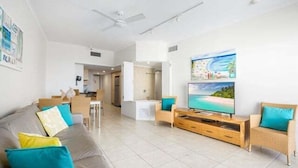 A modern living room with a sofa, TV, and wooden entertainment unit. - 1 Bedroom Balcony Poolside (Kings Beach)