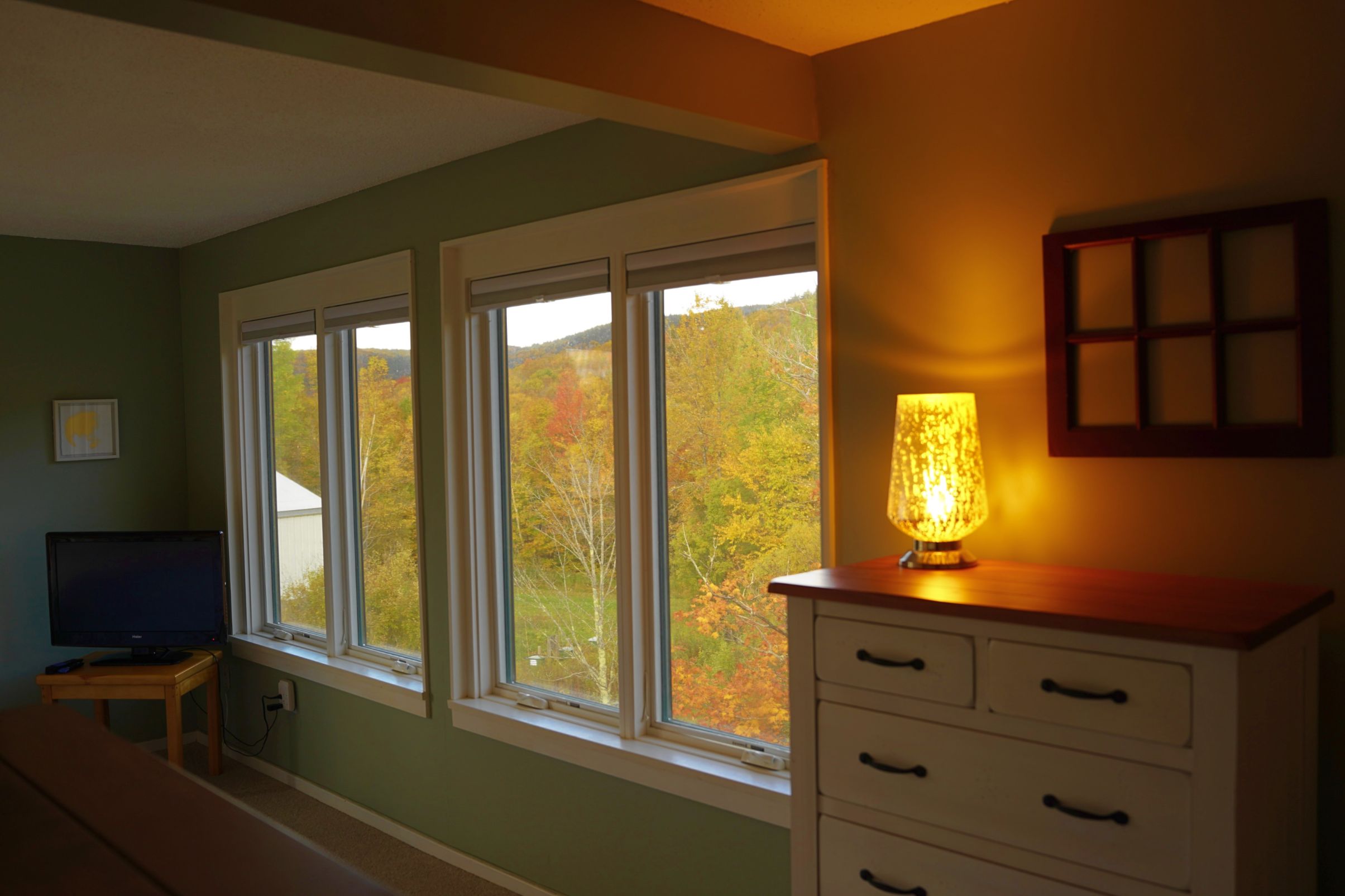 A room with a large window, a desk with a computer, a lamp, and a cabinet.