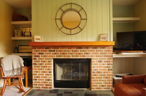 A living room with a brick fireplace, a television, and a cozy seating area. - Cozy mountain condo on family run ski resort, hiking, biking and more.  (Richmond)