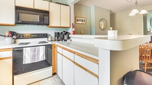 A kitchen with a microwave, stove, coffee maker, and a small island with a sink.