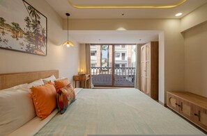 A bedroom with a bed, a nightstand, a lamp, a balcony with a view of buildings, and a door. - Stylish 1bhk in Candolim Pool Gym Near Beach (Candolim)